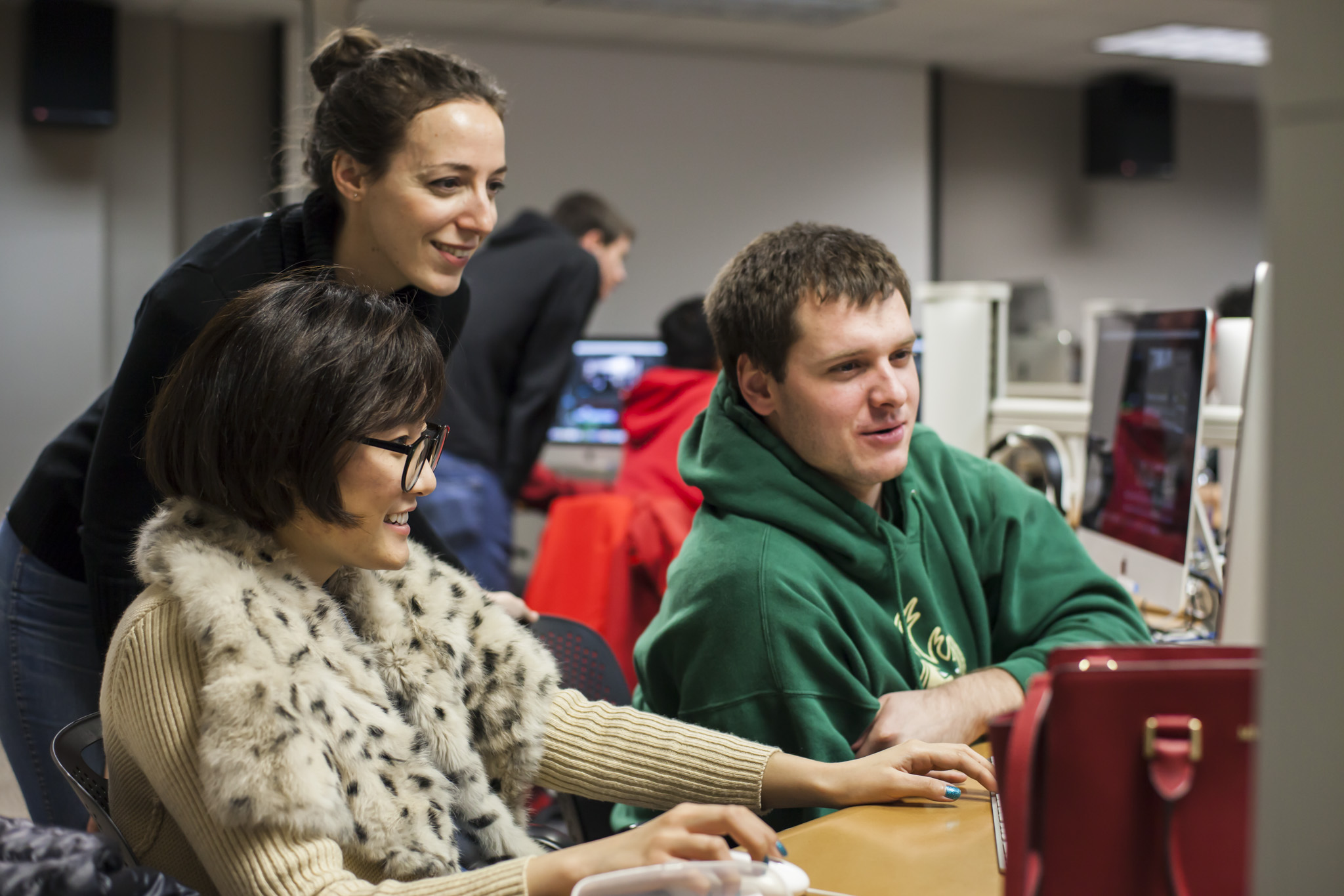 A teaching assistant helps two students editing a video in the Hamel Lab.