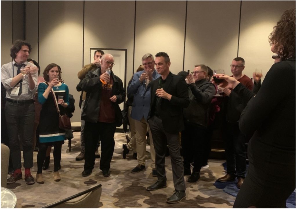 A group of scholars toast and applaud Dr. Robert Asen in a hotel ballroom