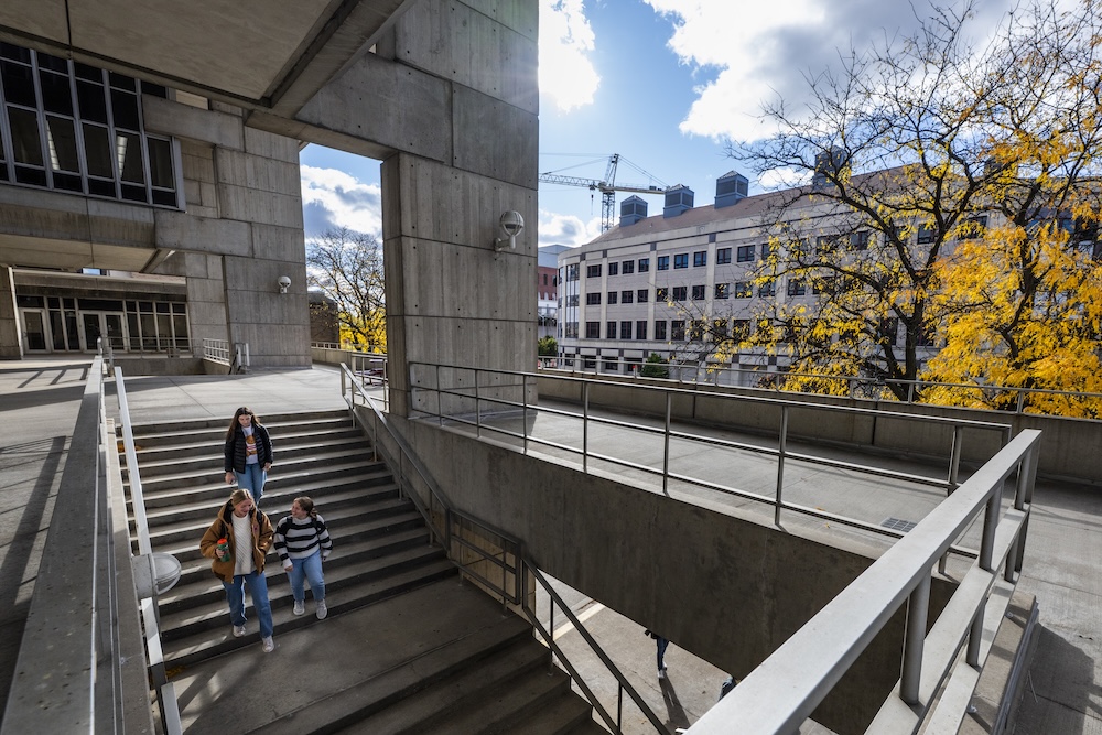 Outdoors of Vilas, three students walk down the stairs on a fall day. 