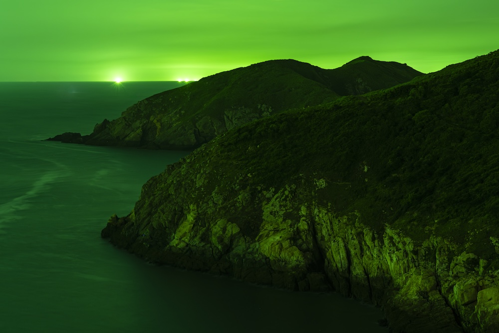 Silhouettes of islands with green fishing lights on the horizon.