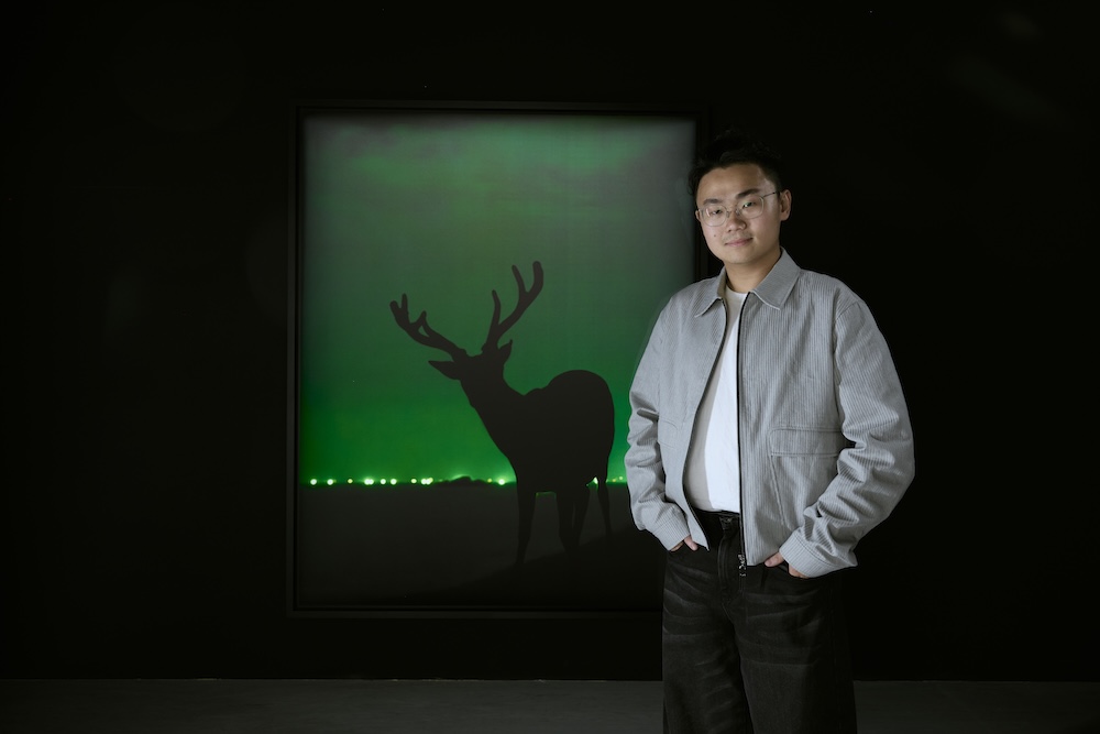 Chang-Ching Su standing in front of a photo of a silhouetted buck for his art exhibit in Taipei.